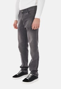 Jeans in denim grigio con una vestibilità slim, caratterizzati da un classico design a cinque tasche, chiusura con bottone e lievi scoloriture. Indossati con sneakers nere.