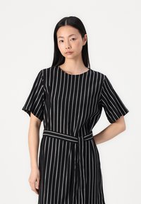 Vestido listrado em preto e branco com mangas curtas, decote redondo e um cinto atado na cintura. Tecido texturizado com linhas verticais.