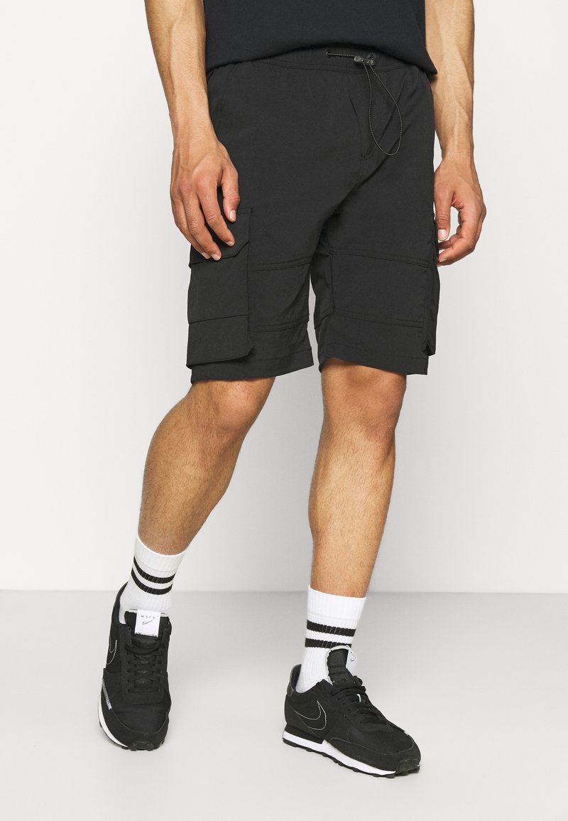 Des shorts cargo noirs en tissu léger présentant de multiples poches latérales, une taille élastique avec cordon de serrage et une coupe décontractée.