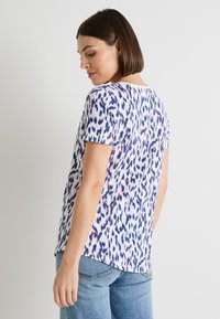 Top de manga corta en tejido ligero, con un estampado animal en tonos rosa, azul y púrpura, cuello redondo y dobladillo ligeramente curvado.
