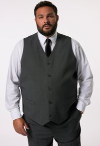 Traje gris de tres piezas con chaleco abotonado, camisa de vestir blanca y corbata negra. Presenta un diseño elegante y un ajuste a medida.