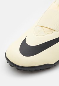 Yellow soccer shoe with a textured surface, featuring a prominent black Nike swoosh logo and a rubber outsole for traction.