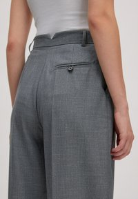 Graue, maßgeschneiderte Hosen mit einer strukturierten Oberfläche, ausgestattet mit einer Gesäßtasche und Knopfdetails, entworfen im geraden Schnitt.