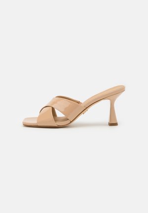 Beige lakleren mule met kruisbandjes en slanke midhoge hak op een effen witte achtergrond.