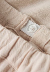 Šviesiai rožinė medžiaga su tekstūruota paviršiumi, su baltu mygtuko užsegimu ir elastinga juosta, demonstruojanti švelnumą ir subtilų raštą.