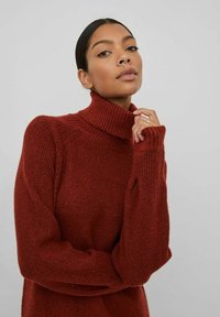 Maglione color ruggine con collo alto, in un motivo a maglia testurizzato, caratterizzato da spalle scese e polsini a costine. Vestibilità ampia e materiale soffice.