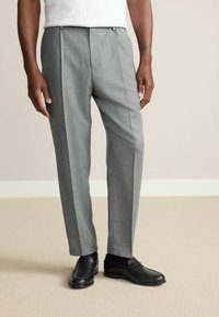 Gray wool trousers with a slim fit, featuring a subtle textured pattern and vertical creases. Paired with black loafers.