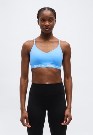 Atletische vrouw die een lichtblauwe Nike sportbeha en hoogwater zwarte legging draagt tegen een effen witte achtergrond.