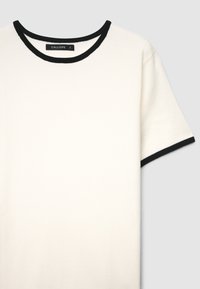 Weißes T-Shirt mit kurzen Ärmeln, einem schwarzen gerippten Rundhalsausschnitt und schwarzen Enden an den Ärmeln, hergestellt aus weichem Material. Das Etikett trägt die Aufschrift "CALLIOPE S."