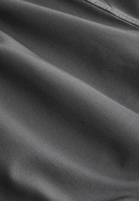 Weiches, dunkelgraues Gewebe mit glatter Textur, das subtilen Glanz und leichte Drapierung zeigt, wodurch sein Fluss und seine Flexibilität hervorgehoben werden.