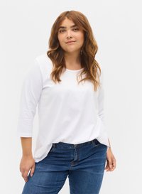 Weißes Longsleeve-Shirt mit rundem Ausschnitt, aus weichem Baumwollstoff gefertigt. Kombiniert mit blauen Jeans, die einen lässigen Stil zeigen.