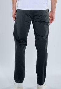 Dunkelgraue Hose aus glattem Stoff, mit gerader Passform, Seitentaschen und elastischem Bund. Tragen mit weißen Sneakers.