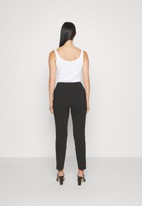 Černé kalhoty na míru se střihovým designem rovné nohavice, s hladkou texturou a dvěma zadními kapsami. Spárované s bílou tílkem.