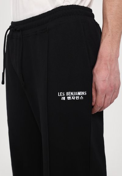 Μαύρες φόρμες με κορδελάκι στη μέση, με λευκή κεντημένη επιγραφή "LES BENJAMINS" στο αριστερό μηρό και λεία υφή.