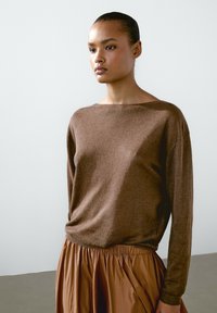 Hnědý, lehký svetr s širokým výstřihem a dlouhými rukávy, kombinovaný s texturovanou hnědou sukní střední délky s plisováním. Hladká tkanina.