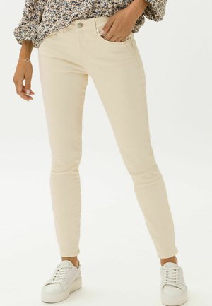 Jean skinny beige clair en tissu de coton mélangé, avec un design classique à cinq poches et des détails de couture subtils. Associés à des baskets blanches.
