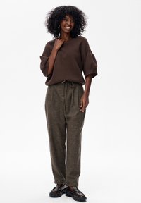 Bruine oversized trui met korte, brede mouwen, gecombineerd met hoge taille, gestructureerde, lichtbruine broeken. Zwarte plateau-schoenen.