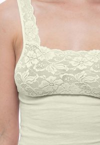 Light-colored tank top featuring a lace overlay at the neckline with floral patterns, made from soft, stretchy fabric.