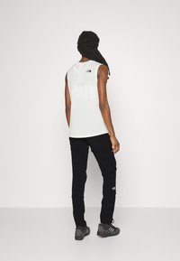 Vit ärmlös träningslinne med en liten svart logga på baksidan, kombinerat med svarta cargobyxor och grå utomhusskor.