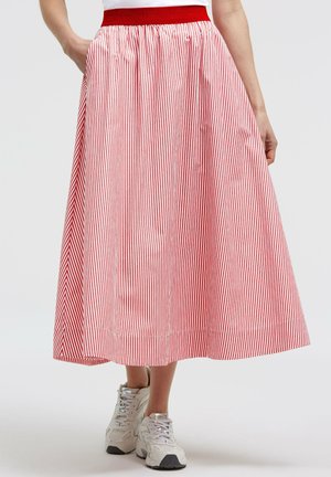 Person wearing a red and white vertical striped midi skirt with a red waistband, white sneakers, and a white top, hands in skirt pockets.