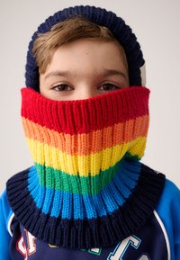 Vícebarevný pletený nákrčník s výraznými pruhy v červené, oranžové, žluté, zelené a modré barvě; doplněný námořnicky modrou žebrovanou čepicí.