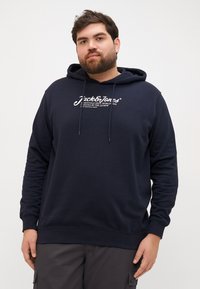 Navy blue hoodie with a front kangaroo pocket, drawstring hood, and white logo text. Features ribbed cuffs and hem, made of soft fabric.