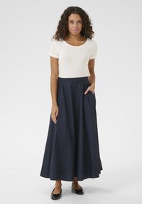 Gonna blu navy, lunga fino al ginocchio, con design plissettato e tasche laterali, abbinata a una camicia aderente color crema. Tessuto morbido, decorazioni minime.