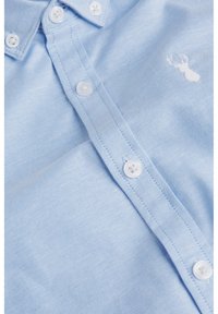 Chemise bleu clair boutonnée en tissu texturé, dotée d'un col classique, de boutons blancs et d'un logo brodé sur la poitrine.