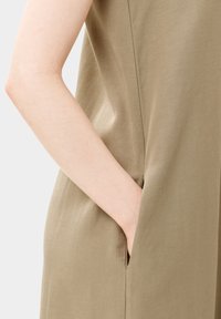 Vestido beige con una textura suave, que presenta un bolsillo lateral y un corte relajado; diseño minimalista que enfatiza la sencillez.