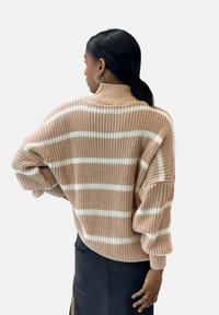 Strickpullover in hellem Pfirsich mit weißen Streifen, ausgestattet mit einem hohen Kragen und übergroßen Ärmeln. Die Textur ist dick und gerippt.