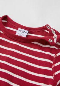 Punainen ja valkoinen raidallinen puuvillapaita, jossa on pyöreä pääntie, ja jossa on nepparit yhdellä olalla sekä etiketti, joka ilmoittaa koon 1,5-2 vuotta.