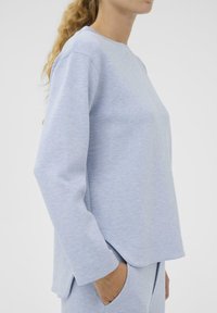 Hele sinine pikkade varrukatega dressipluus ümarate alläärega. Valmistatud pehmest materjalist, millel on õrn tekstuuriline muster.