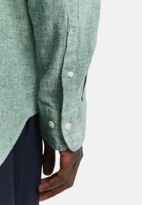 Lichtgroene linnen blouse met lange mouwen, voorzien van twee knoopsluitingen bij de manchetten en zijinsnodingen voor een ontspannen pasvorm.