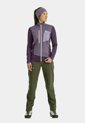 Fleece jacket in shades of purple with zip pockets, paired with green outdoor pants. Features a fitted design and long sleeves.
