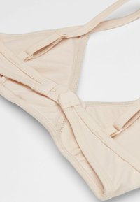 Béžová podprsenka s měkkou tkaninou, nastavitelnými ramínky a zapínáním na háček a oko. Design zahrnuje bezešvé okraje a lehké vycpávky pro pohodlí.