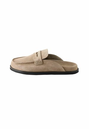 Béžové semišové slip-on mule s čiernou podrážkou a prešívaním v štýle mokasínov na hornej časti.