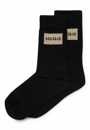 Calze nera in cotone con un bordo a coste e una toppa rettangolare beige con la scritta "HUGO" in lettere nere. Texture liscia.