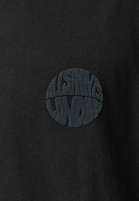 Sort bomulds T-shirt med et rundt, tekstureret mørkt logo, der læser "ALLSAINTS LONDON" i fed, stiliseret skrift på brystet.