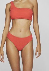 Bikini rojo de canalé con parte superior de un solo hombro y parte inferior de cintura alta. El material parece elástico; ambas piezas presentan una superficie texturizada.