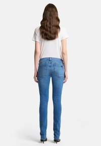 Blauwe jeans met een slim fit, gemaakt van denim. Kenmerken zijn achterzakken en een middelhoge tailleband. Gemaakt in combinatie met een wit t-shirt.