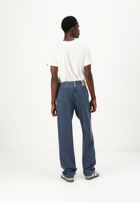 Relaxed-fit, vervaagde blauwe spijkerbroek met een rechte snit, vijf zakken en een bruine leren patch op de achterkant van de tailleband. Gepaard met een wit t-shirt.