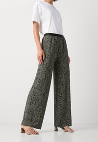 Pantalons larges à motif noir et crème, taille élastique, associés à un t-shirt blanc et des sandales à brides crème, mettant en avant un design décontracté.