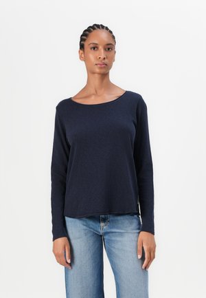 Maglia a maniche lunghe blu navy con scollatura rotonda, vestibilità morbida, texture delicata e motivo sottile; abbinata a jeans azzurri chiari.