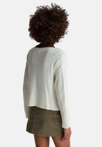 Weißer gestrickter Pullover mit geripptem Saum und Bündchen, mit einem leicht verkürzten Schnitt. Kombiniert mit einem olivgrünen Cordrock.