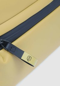 Borsa gialla dalla texture liscia, dotata di una cerniera scura e di una tracolla nera con dettaglio a contrasto giallo e logo.