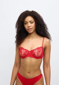 Crveni čipkasti balconette grudnjak s prozirnim mrežastim košaricama, cvjetnim vezom, podesivim remenčićima i malim mašnicom u sredini.