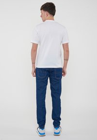 T-shirt bianca in cotone con maniche corte, abbinata a jeans in denim blu con cuciture arancioni e una vestibilità slim. Sneakers con accenti blu.