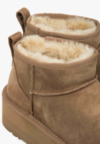 Brązowe botki zamszowe z miękkim kremowym ociepleniem z owczej wełny, zaokrąglonym czubkiem i wzmocnioną tylną zakładką ułatwiającą zakładanie. Gruba podeszwa.