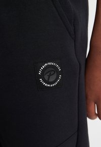 Sorte bomulds sweatpants med en struktureret sort lap, der har et rundt logo og brandnavn på den højre sidelomme.