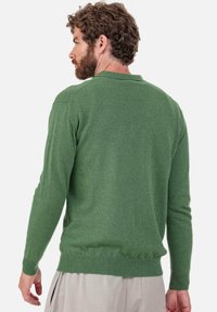 Pull en maille verte à manches longues, avec poignets et ourlet côtelés. Texture douce, design minimaliste et coupe ajustée. Doté d'un col classique.